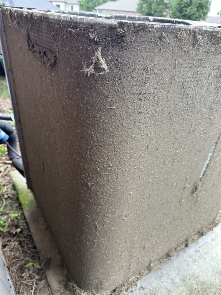 An outdoor AC unit’s coil caked with dust, lint and grass, before cleaning