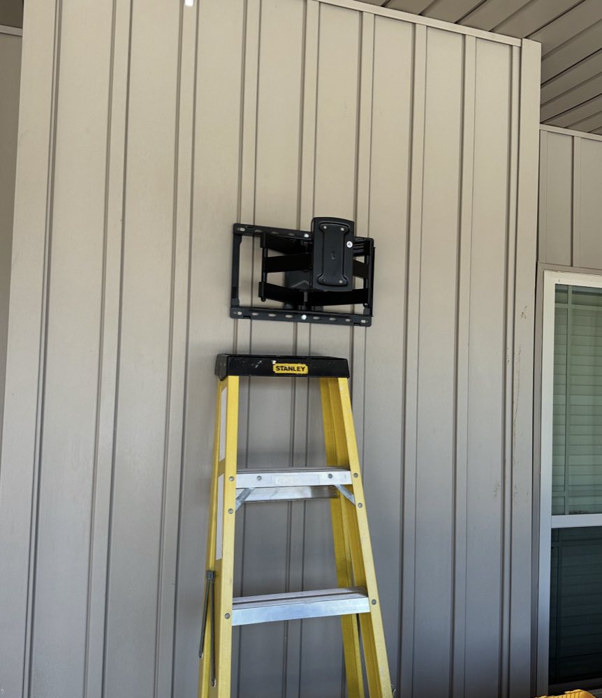 A full-motion TV mount installed on a covered porch wall