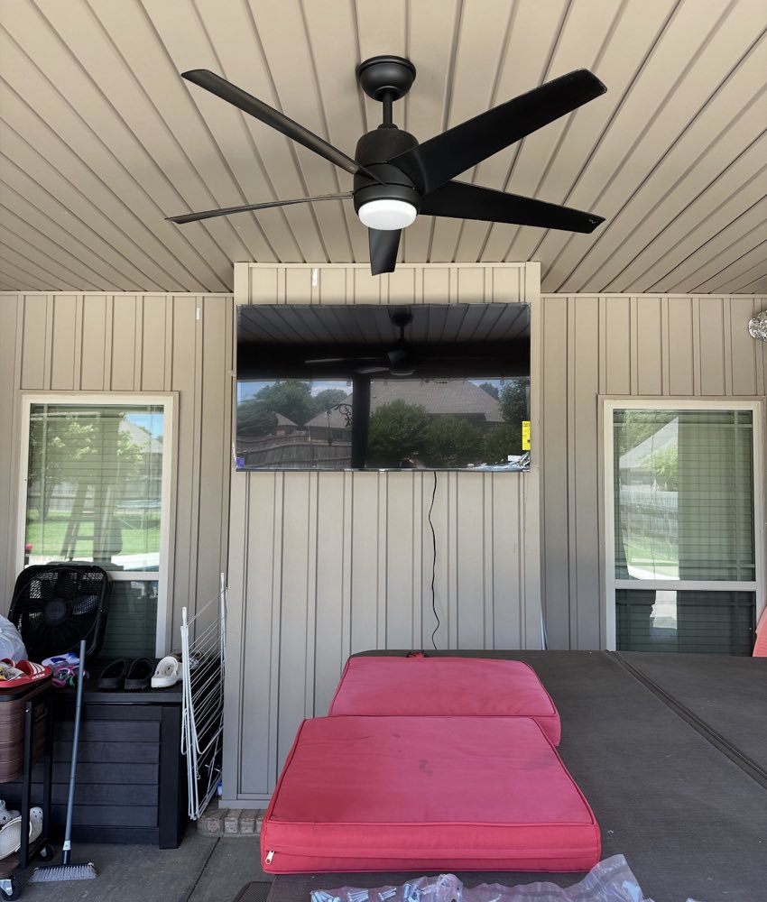 The TV hung on the porch wall below the ceiling fan